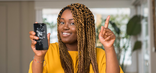 Wall Mural - African american woman showing broken smartphone surprised with an idea or question pointing finger with happy face, number one