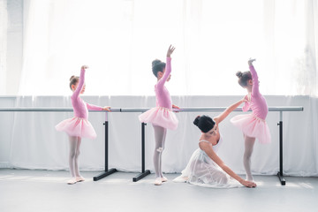 Wall Mural - side view of young ballet teacher exercising with kids in ballet school