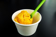 Scoop of mango ice cream in paper cup with plastic spoon isolated