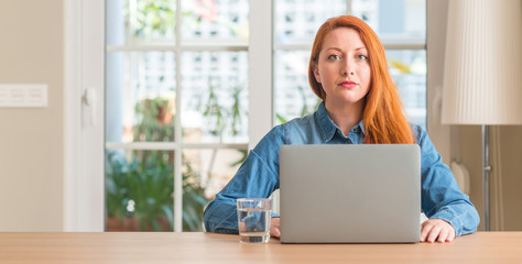 Sticker - Redhead woman using computer laptop at home with a confident expression on smart face thinking serious