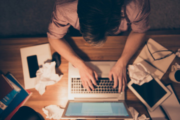 Wall Mural - Upper angle of hard worker, attractive, busy man holding hands on keypad, having crumpled drafts on the table, taking work at home, working at night time, sitting in workplace, workstation