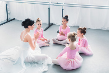 Wall Mural - high angle view of kids in pink tutu skirts and young ballet teacher sitting together in ballet school