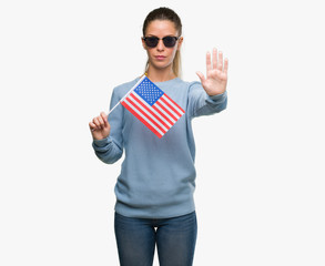 Poster - Beautiful young woman holding USA flag with open hand doing stop sign with serious and confident expression, defense gesture