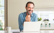 © Krakenimages.com - Middle age man using laptop at home with a happy face standing and smiling with a confident smile showing teeth