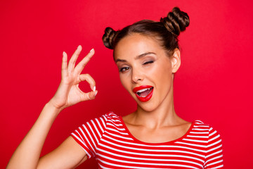 Wall Mural - Close up portrait of happy girl with wide open mouth and wink eye gesturing ok sign isolated on vivid red background