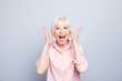 Old adult blonde glad excited cheerful astonished lady smiling, laughing, screaming, raising hands to cheeks, opened mouth, over grey background, isolated