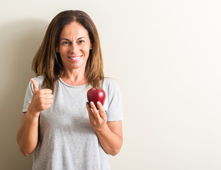 Middle age woman holding a green apple happy with big smile doing ok sign, thumb up with fingers, excellent sign