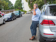 Man is standing in the street next to car and talking on the phone