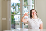 Fototapeta Panele - Down syndrome woman at home smiling and confident gesturing with hand doing size sign with fingers while looking and the camera. Measure concept.
