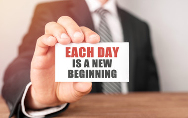 Poster - businessman holding a card with text each day is a new beginning