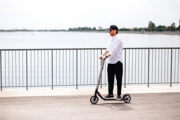 Modern man in stylish black and white outfit riding electric scooter in the city