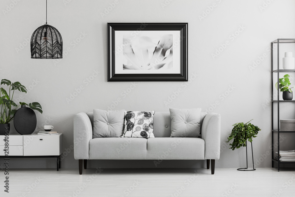 Black industrial bookcase and a plant stand next to an upholstered sofa in a gray living room interior with place for a coffee table. Real photo - obrazy, fototapety, plakaty 