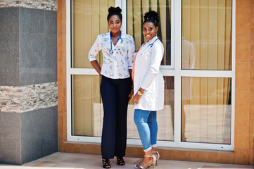 Wall Mural - Two african american doctors female at lab coat with stethoscope posed outdoor against clinic.