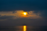 Fototapeta Morze - Dramatic light mood with orange illuminated clouds and the sun as a fiery ball during a sunrise over the Baltic Sea in Bansin on usedom, Germany