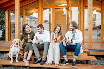 Wall Mural - Young friends enjoying evening time sitting together with dog on the terrace of the modern wooden house