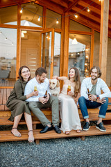 Wall Mural - Young friends enjoying evening time sitting together with dog on the terrace of the modern wooden house