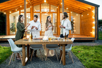 Wall Mural - Friends having a dinner with pizza on the backyard of the modern house decorated with lights during the evening time outdoors