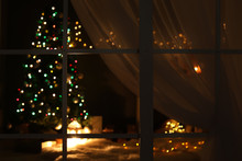 Blurred View Of Stylish Living Room Interior With Christmas Lights At Night Through Window