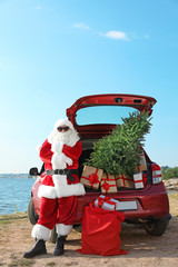 Wall Mural - Authentic Santa Claus near red car with gift boxes and Christmas tree on beach