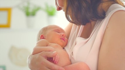 Fototapete - Mother and her newborn baby. Happy mom kissing and hugging her baby. Maternity concept. Motherhood. Happy family. Adoption. Slow motion 4K UHD video 3840x2160