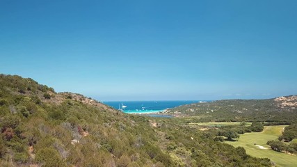 Wall Mural - Aerial view of a emerald and transparent Mediterranean sea with a white beach and some yachts in the background. Green hills and a golf course in the foreground. Costa Smeralda, Sardinia, Italy.