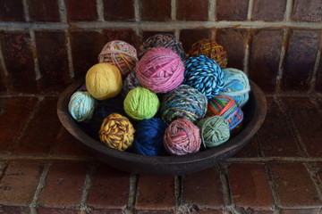 Wall Mural - This is a wood bowl on a red brick background filled with a variety of different colored hand spun yarn made from the wool of sheep.