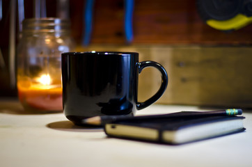 Wall Mural - A blank black coffee mug on the work bench under the candle light.