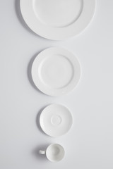 Poster - Top view of arranged various plates and cup in row on white table, minimalistic concept