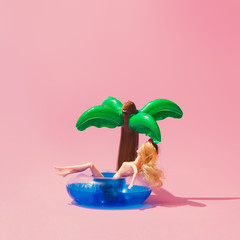 Wall Mural - tropical palm inflatable toy with doll on pink background. creative minimal beauty summer concept.