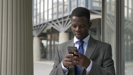 attractive black african business man walking and typing on his smartphone