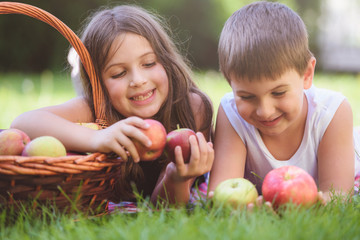 Cute little boy and girl lying in grass with apple basket