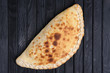 Fresh baked pizza calzone on dark wooden table, top view.