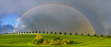 Fototapeta Tęcza - double, beautiful, multi-colored rainbow after passing a spring downpour over a green field