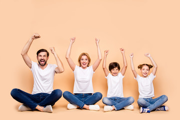 Poster - Young smiling family, bearded father, blonde mother, little boy and girl wearing blue jeans and white T-shirts, sitting in odrer of hierarchy in lotus pose raising up hands