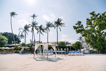 Wall Mural - Wedding venue with minimal flower decoration on the beach, white cover chairs with blue stripes sash organza, long coconut palm tree background