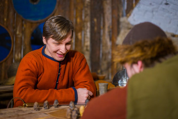 Two men in russian ethnic suit playing medieval popular strategy board game - tafl. Folk, competition and traditional concept