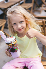 Wall Mural - selective focus of smiling little child holding dessert and doing thumb up gesture