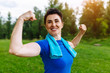Smiling Senior woman flexing muscles outdoor in park. Elderly female showing biceps. Heathy life style concept. Copyspace.