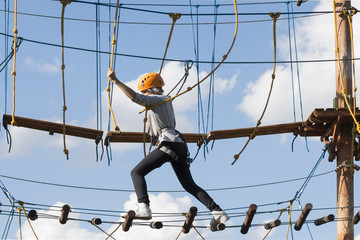 A school girl climbs in an adventure rope park on a summer day