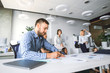 © pantovich - Office worker in the foreground sitting at the table making records in documents on the background of business colleagues