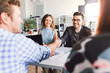 © pantovich - Businessmen shake hands with each other sitting at the table with colleagues