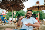 Fototapeta Miasto - Portrait of a young handsome man drinking coffee at the beach cafe.