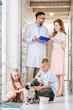 © LIGHTFIELD STUDIOS - veterinarian showing something in clipboard to woman, kids playing with pug dog at veterinary clinic