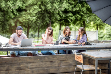 Wall Mural - Young people sitting at the big table working or studying with laptops and documents outdoors in the park