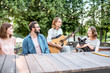 © rh2010 - Young friends having fun together playing a guitar sitting at the table outdoors in the park