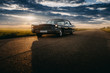 Black retro vintage muscle car is parked at countryside asphalt road at golden sunset