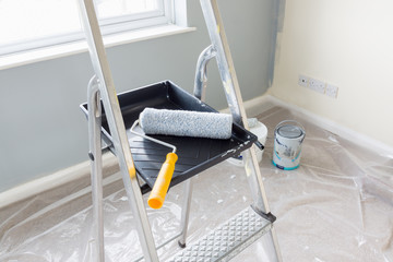 painting and decorating with a roller and tray on a set of metal step ladders with cans of paint and
