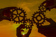 © gerasimov174 - gears in the hands of a group of people against the background of the evening sky. teamwork concept