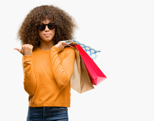 Canvas Print - African american woman holding shopping bags pointing with hand and finger up with happy face smiling