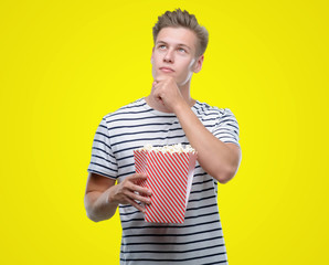 Sticker - Young handsome blond man eating popcorn serious face thinking about question, very confused idea